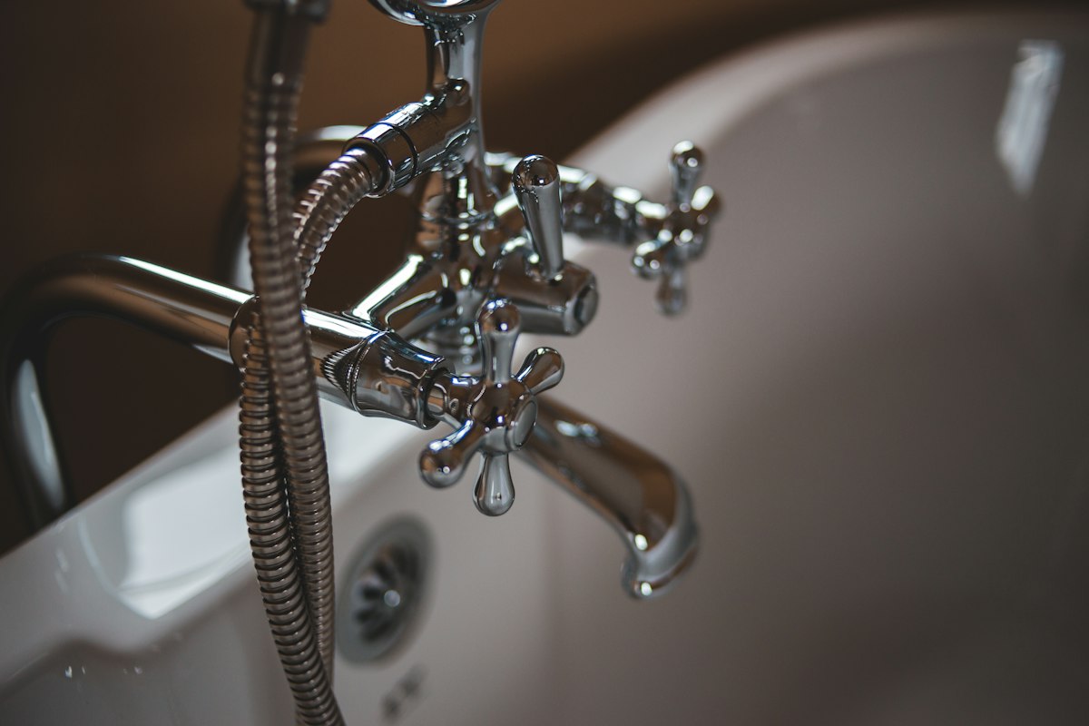 Chrome bath faucet and hand shower above a white bathtub